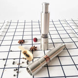 Two silver pepper mills on a checkered tablecloth with peppercorns and star anise.